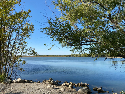 A serene lake view surrounded by trees and rocks under a clear blue sky.