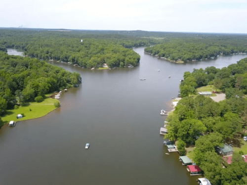 Aerial view of a serene lake surrounded by lush greenery and houses along the shoreline.