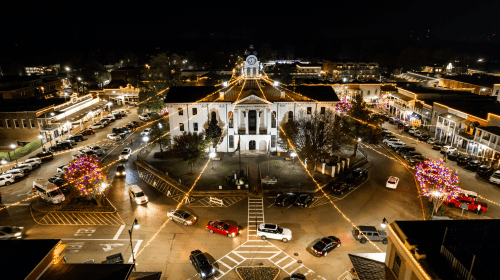 Aerial view of a beautifully lit town square at night, featuring a historic building and festive decorations.