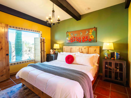 Cozy bedroom with a wooden bed, colorful walls, a cactus view, and warm lighting from bedside lamps.