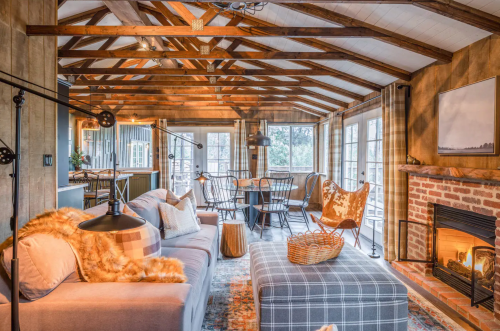 Cozy living room with wooden beams, a fireplace, comfortable seating, and large windows for natural light.