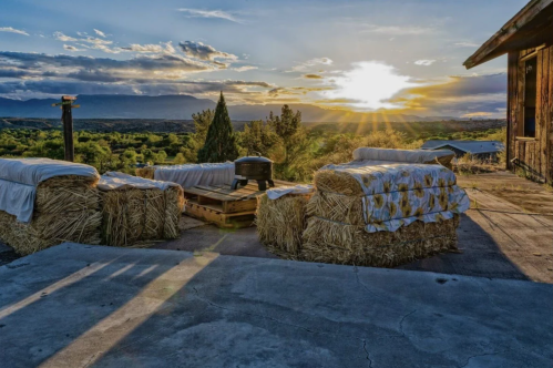 A cozy outdoor seating area made of hay bales, with a stunning sunset and mountains in the background.