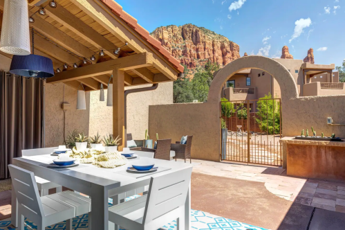 A patio with a dining table, chairs, and a view of red rock formations under a clear blue sky.