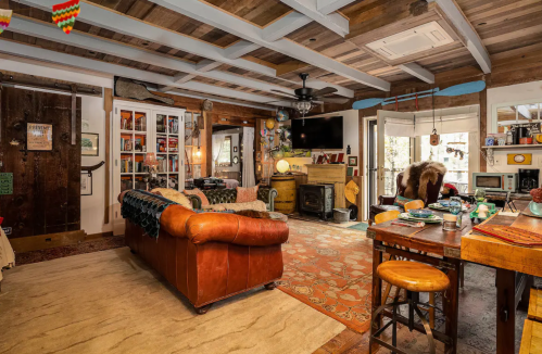 Cozy living room with a leather sofa, wooden beams, a fireplace, and eclectic decor, creating a warm, inviting atmosphere.