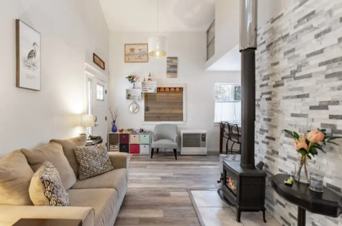 Cozy living space with a beige sofa, decorative wall, and a wood stove, featuring modern decor and natural light.