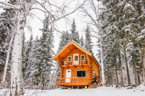 A cozy log cabin surrounded by snow-covered trees in a winter landscape.