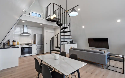 Modern open-concept living space with a spiral staircase, kitchen, dining table, and cozy seating area.