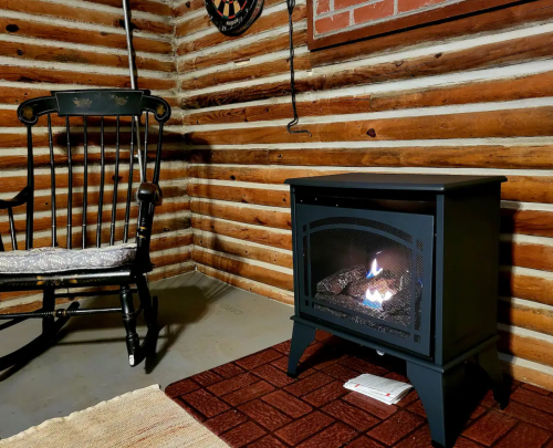 A cozy corner with a black gas stove, a rocking chair, and log cabin walls, creating a warm atmosphere.