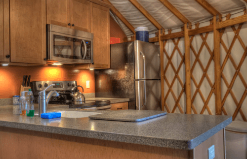 A cozy kitchen inside a yurt, featuring wooden cabinets, stainless steel appliances, and a spacious countertop.