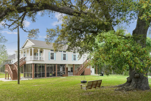 A spacious two-story house with a large yard, surrounded by trees and a bench in the foreground.