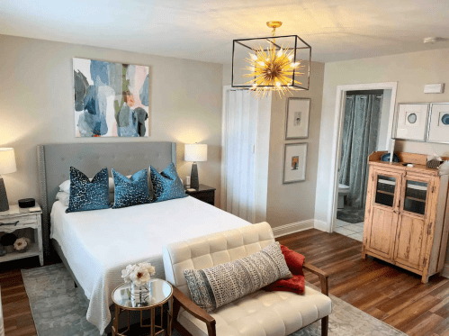 Cozy bedroom featuring a bed with decorative pillows, a stylish light fixture, and a vintage wooden cabinet.