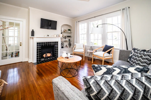 Cozy living room with a fireplace, modern decor, a round coffee table, and large windows letting in natural light.