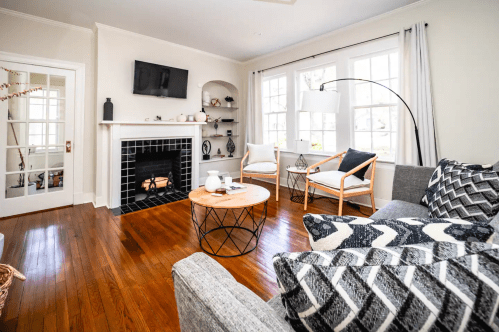 Cozy living room with a fireplace, modern decor, a round coffee table, and large windows letting in natural light.