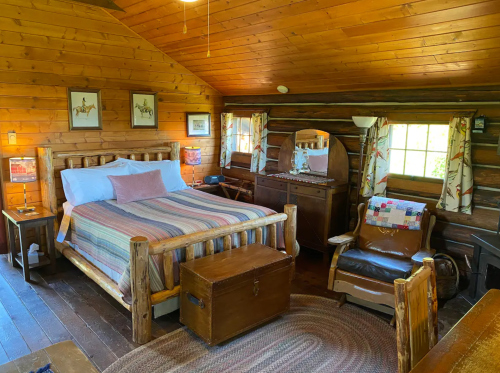 Cozy log cabin bedroom with wooden furniture, a striped blanket on the bed, and warm, rustic decor.
