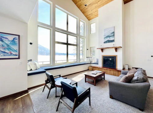 Bright, modern living room with large windows, a fireplace, and cozy seating overlooking a scenic view.