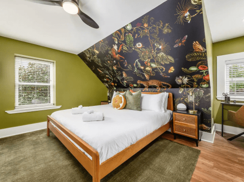 Cozy bedroom with a sloped ceiling, floral wallpaper, a wooden bed, and green walls, featuring natural light from windows.