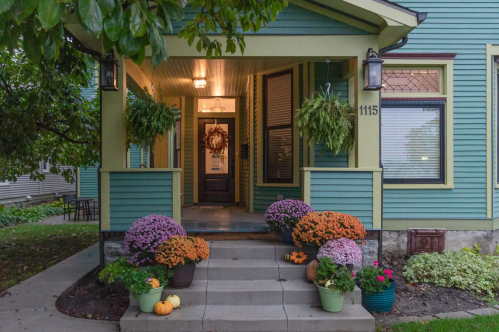 A charming porch with colorful potted flowers, pumpkins, and hanging plants, welcoming visitors to a green house.
