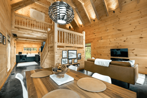 Cozy wooden cabin interior featuring a dining area, living space, and loft with modern furnishings and natural light.