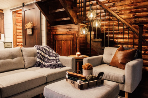 Cozy living room with a gray sofa, armchairs, wooden accents, and warm lighting under a staircase.