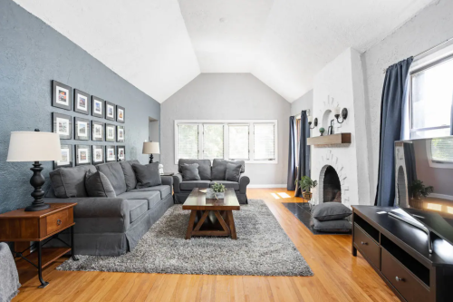 Cozy living room with gray walls, a large sectional sofa, a coffee table, and a fireplace, featuring natural light and decor.
