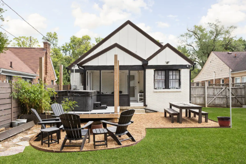 A backyard with a hot tub, wooden seating, and a grassy area, featuring a charming house in the background.