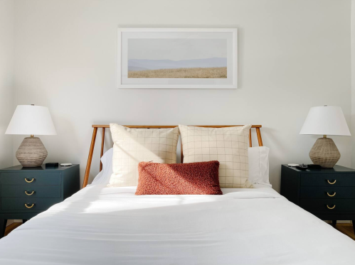 A cozy bedroom featuring a bed with decorative pillows, two lamps, and a framed landscape above.
