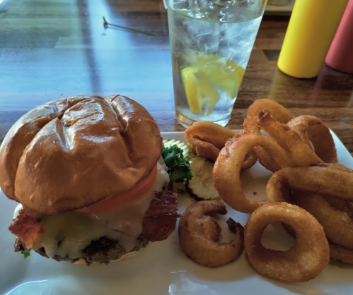 A burger with lettuce, tomato, and cheese, served with onion rings and a glass of water with lemon.