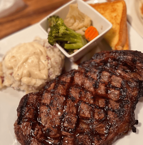 A grilled steak served with mashed potatoes, mixed vegetables, and a slice of bread on a white plate.