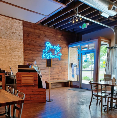 Interior of a restaurant with wooden walls, a neon sign reading "Stoney's Restaurant," and a welcoming entrance.