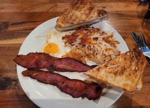 A plate of breakfast featuring crispy bacon, a sunny-side-up egg, hash browns, and toasted bread.