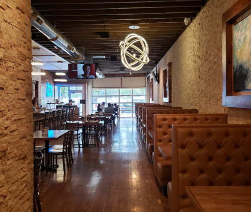 Interior of a restaurant featuring wooden tables, booths, and modern lighting, with a view of patrons dining.