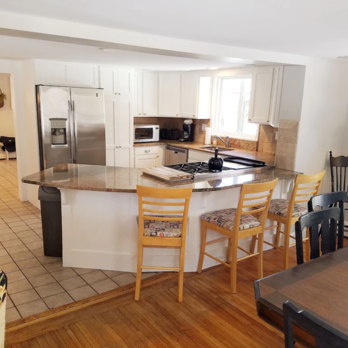 Bright kitchen with a granite island, bar stools, stainless steel appliances, and a dining area in the background.