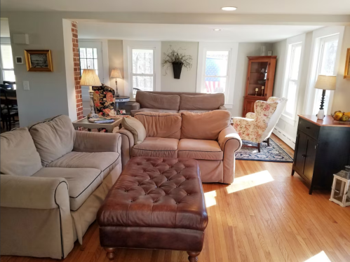 Cozy living room with beige sofas, a brown ottoman, and large windows letting in natural light.