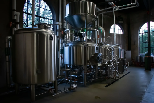 Industrial brewing equipment in a dimly lit space, featuring stainless steel tanks and pipes.