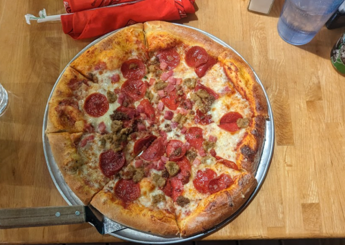 A large pizza topped with pepperoni, sausage, and cheese on a wooden table.