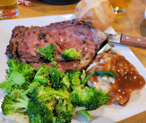 A plate with a large slice of roast beef, broccoli, mashed potatoes with gravy, and a roll.