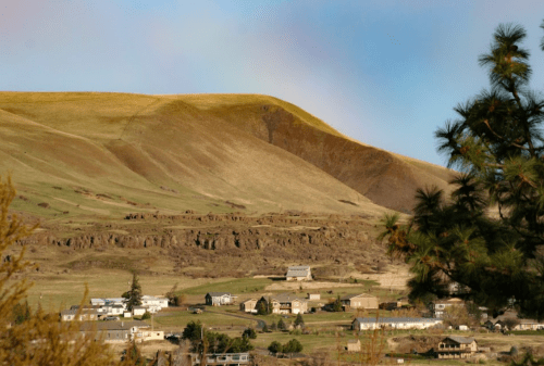 A scenic landscape featuring rolling hills, a small town, and a clear sky with a hint of a rainbow.