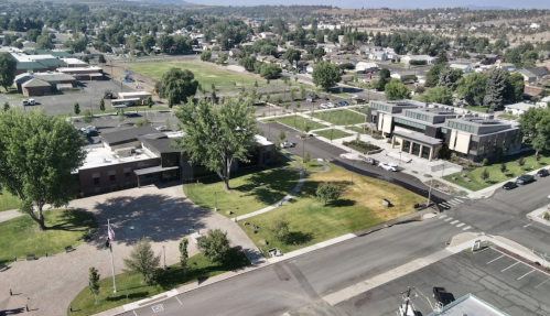 Aerial view of a park and buildings in a small town, featuring green spaces and pathways.