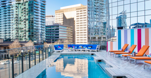 Rooftop pool area with orange lounge chairs, colorful wall, and city skyline in the background.
