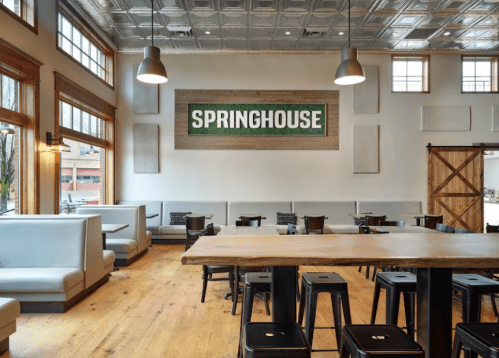 Interior of a modern restaurant featuring wooden floors, booths, and a large "SPRINGHOUSE" sign on the wall.