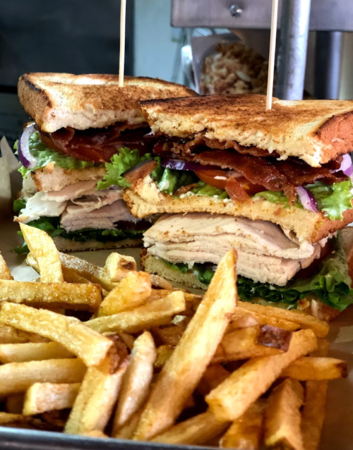 A stacked sandwich with turkey, bacon, lettuce, tomato, and onion, served with a side of golden French fries.