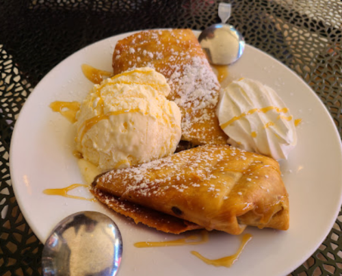 A plate with three crispy pastries, a scoop of vanilla ice cream, whipped cream, and drizzled caramel sauce.