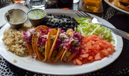 A plate of tacos with purple cabbage, black beans, rice, lettuce, and diced tomatoes, accompanied by sauces.