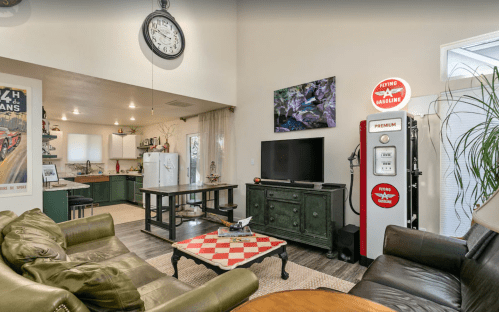 Cozy living room with a vintage gas pump, TV, and kitchen area, featuring a green sofa and a checkered coffee table.
