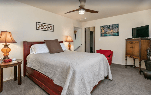 Cozy bedroom with a queen bed, two lamps, a red chair, and a TV, featuring neutral tones and a warm atmosphere.