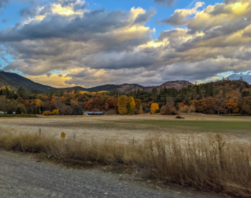 A scenic landscape featuring rolling hills, colorful autumn trees, and a cloudy sky at sunset.