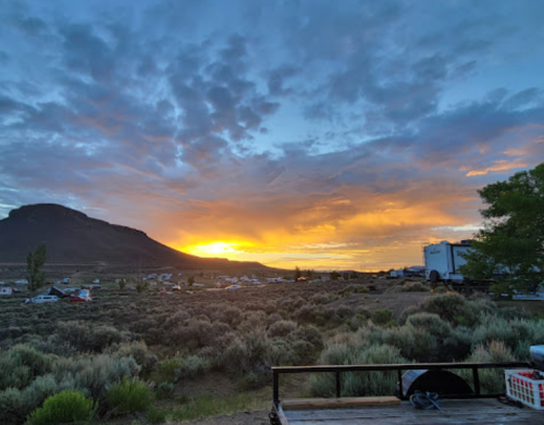 A scenic sunset over a mountainous landscape, with clouds and a campsite in the foreground.