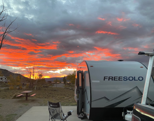 A camper labeled "FREESOLO" sits under a vibrant sunset with dramatic clouds in the background.