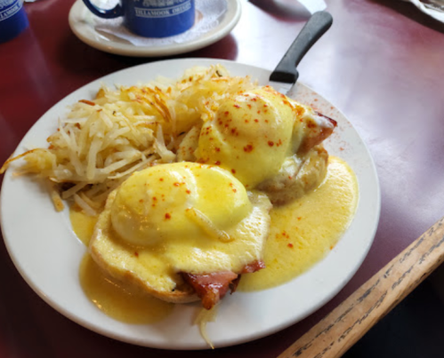 A plate of eggs Benedict with hollandaise sauce, served with hash browns on the side.
