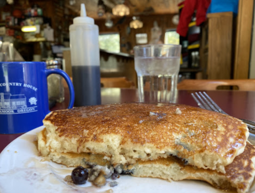 A plate with a half-eaten pancake, a blue mug, a glass of water, and a squeeze bottle in a cozy restaurant setting.